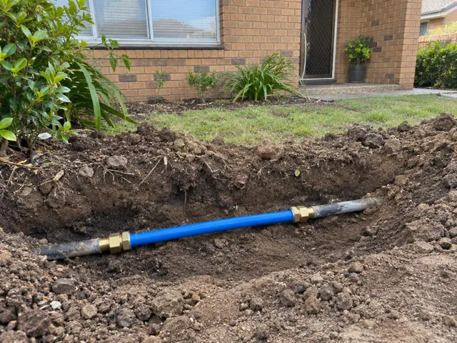 Exposed blue water pipe repair in a dug trench beside a brick house in Bella Vista